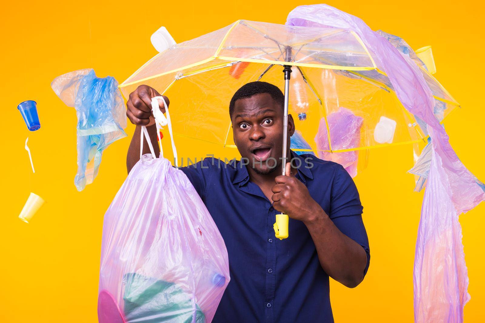 Problem of trash, plastic recycling, pollution and environmental concept - surprised man carrying garbage bag on yellow background.