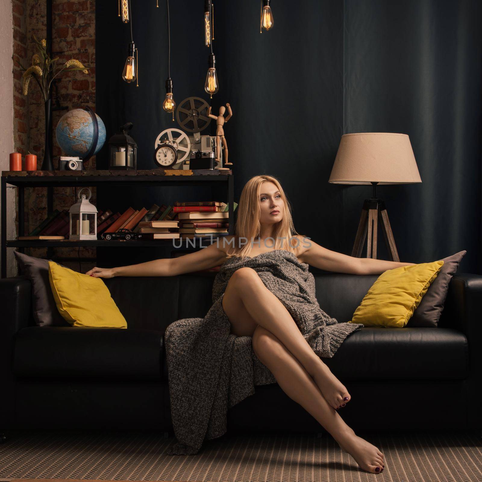 winter concept - young woman sitting on sofa in warm blanket