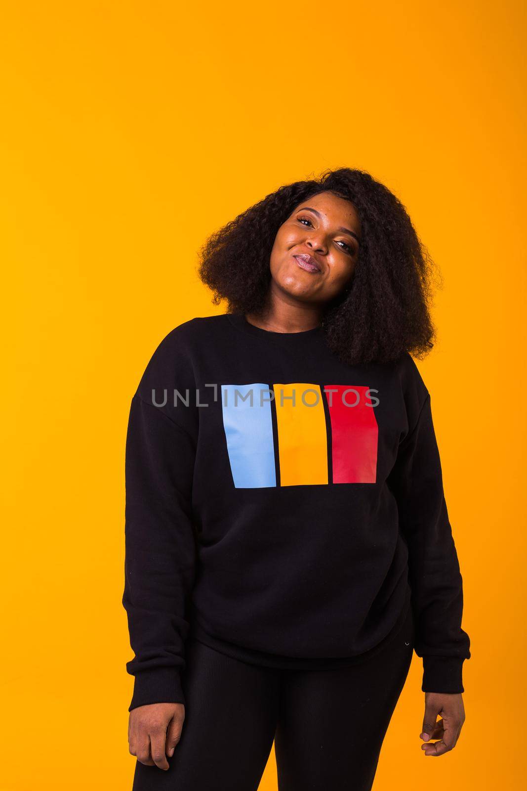 Youth street fashion concept - Confident sexy black woman in stylish sweatshirt having fun on yellow background. by Satura86