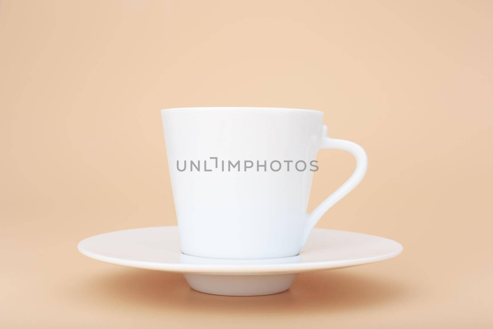 Close up of white ceramic coffee cup with saucer against pastel beige background with copy space by Senorina_Irina