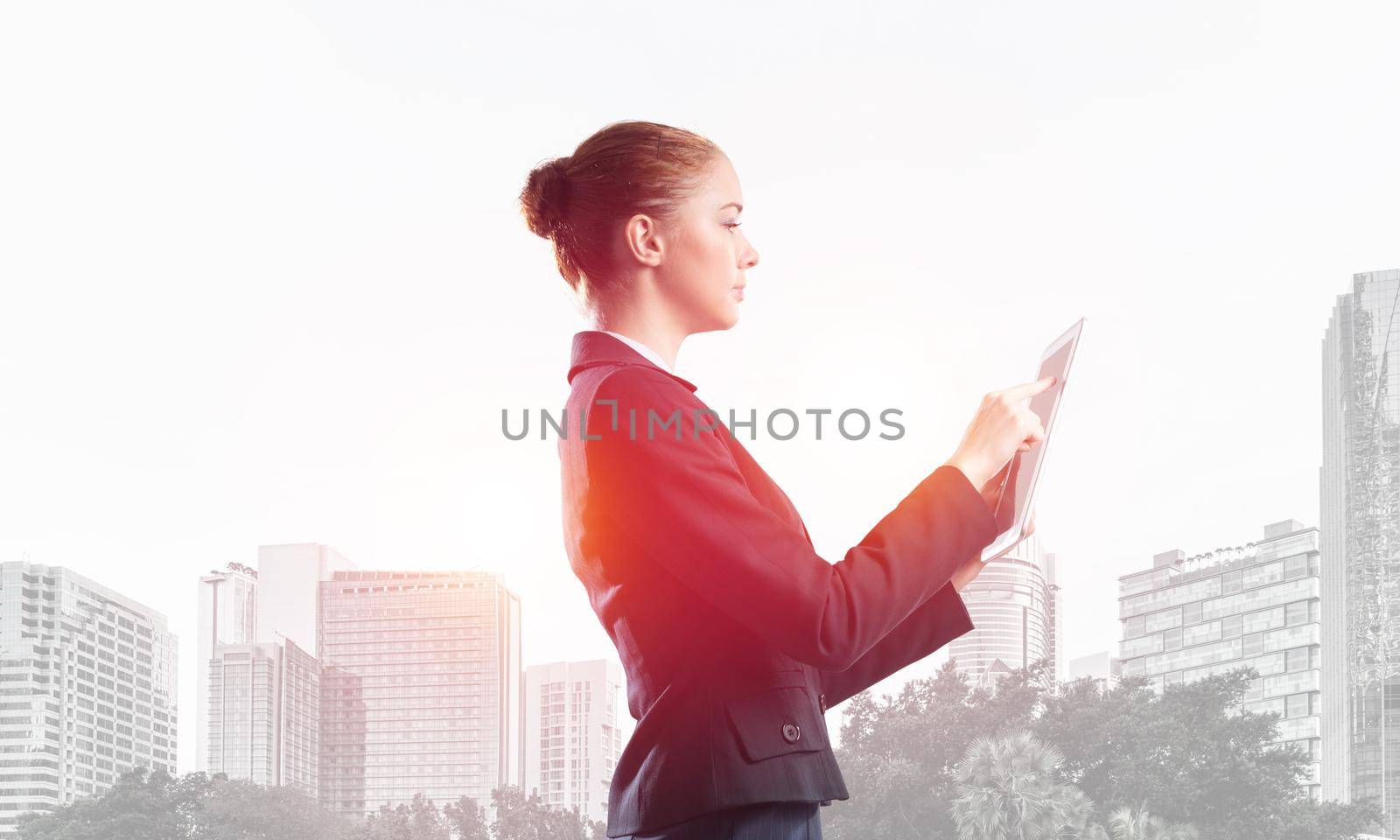 Young businesswoman using tablet computer. Double exposure concept with modern cityscape and beautiful woman in business suit. Digital technology in property management and development company.