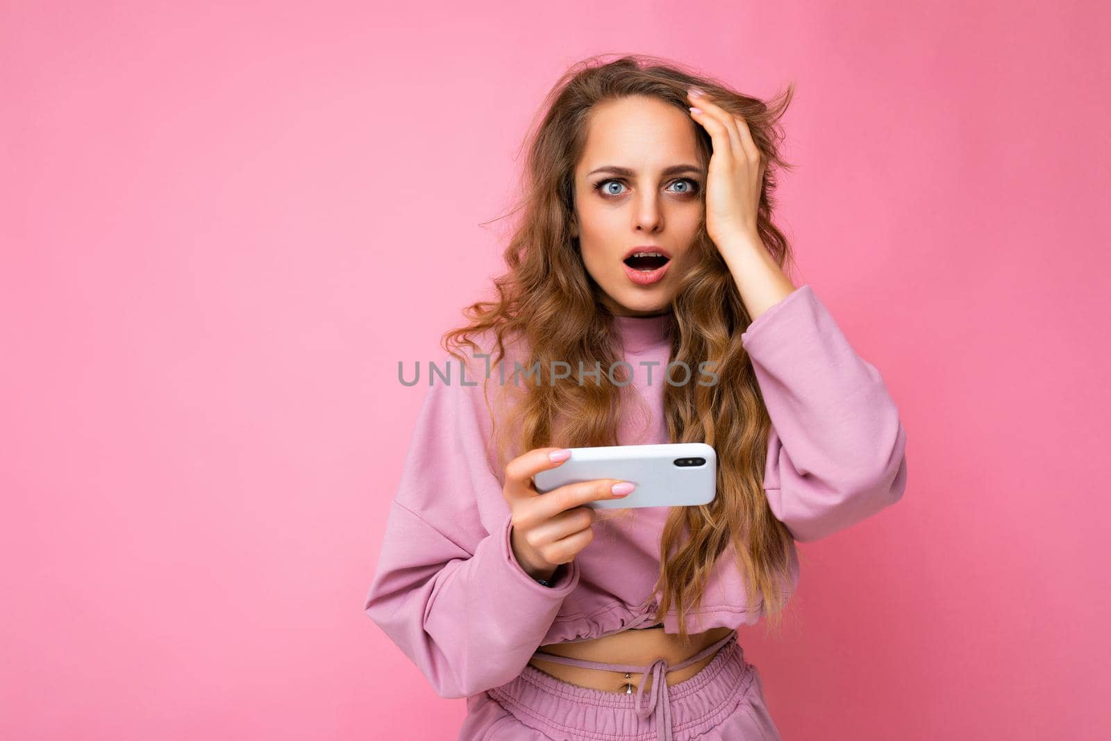 Photo of attractive crazy amazed surprised young woman wearing casual stylish clothes standing isolated over background with copy space holding and using mobile phone looking at camera.