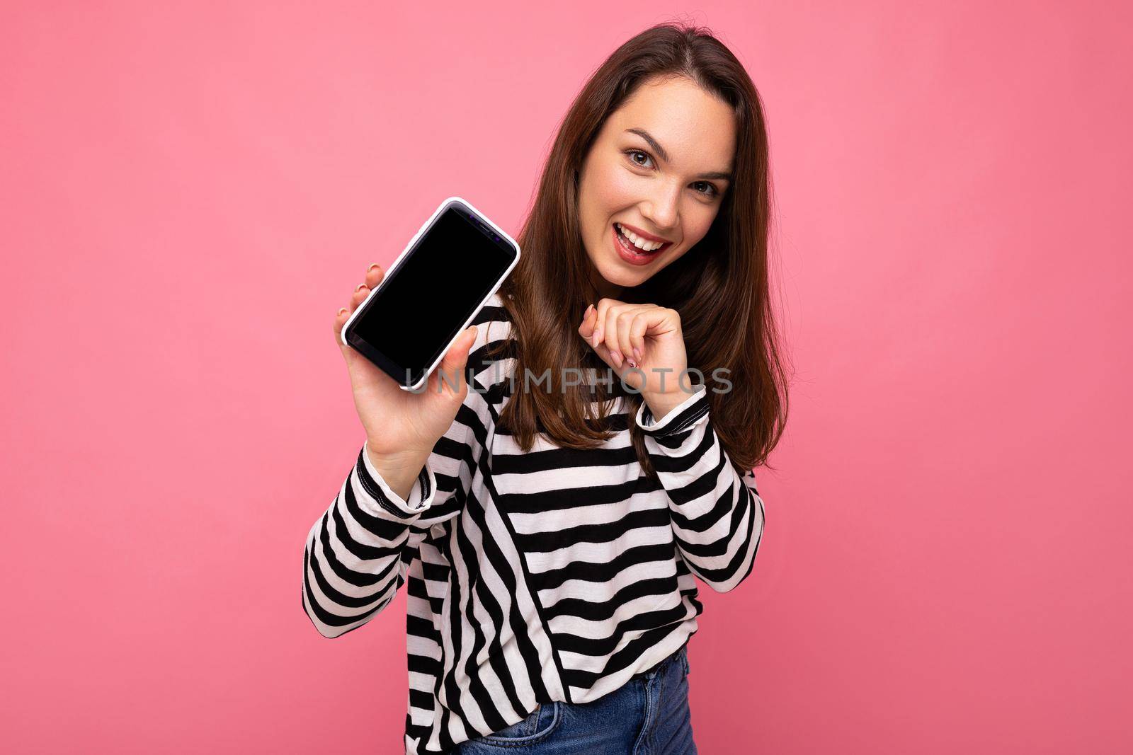 Charming funny adult female person wearing striped sweater isolated over background with copy space looking at camera showing mobile phone screen.