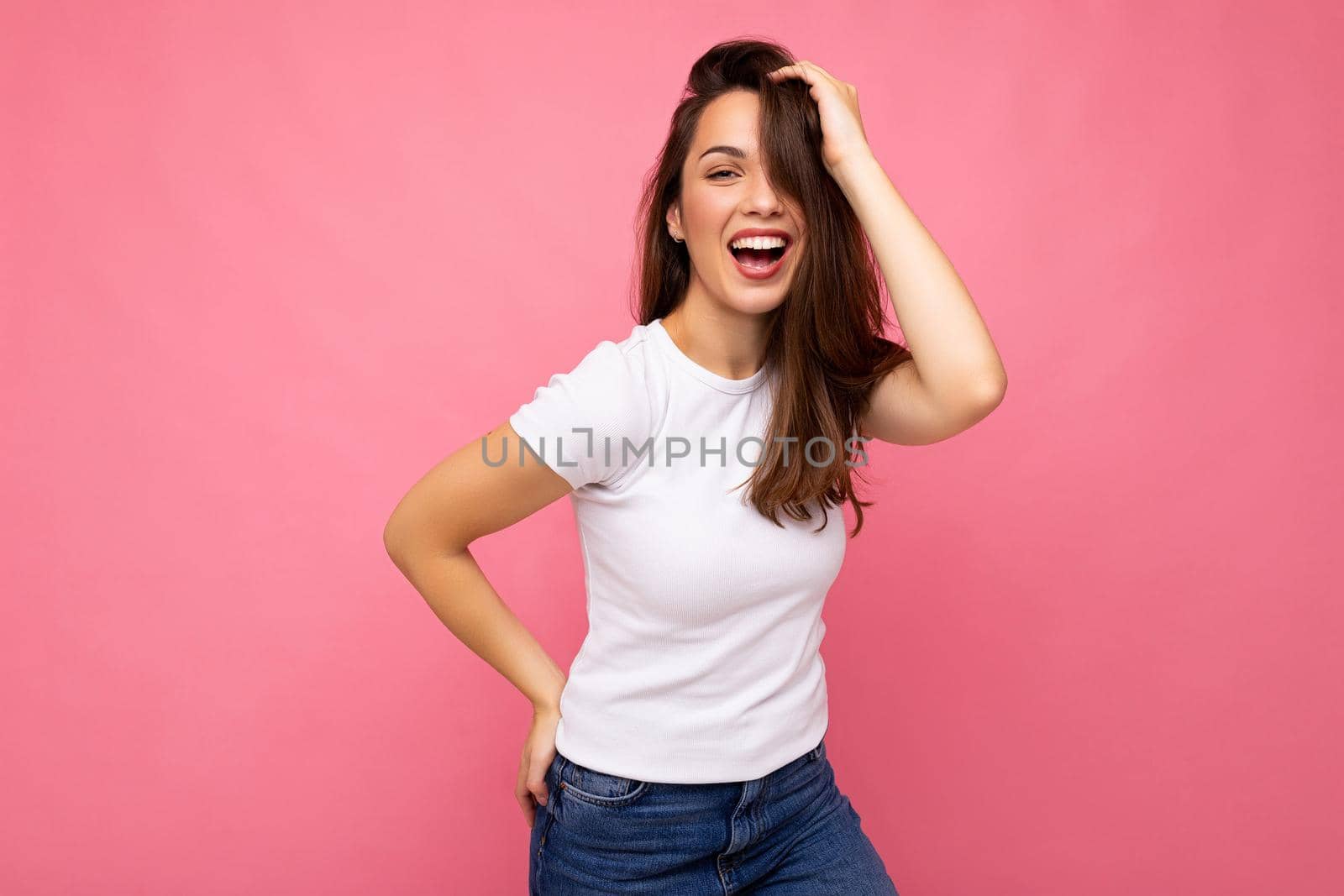 Photo portrait of young beautiful smiling hipster brunette woman in white t-shirt with mockup. Sexy carefree female person posing isolated near pink wall with empty space in studio. Positive model with natural makeup by TRMK
