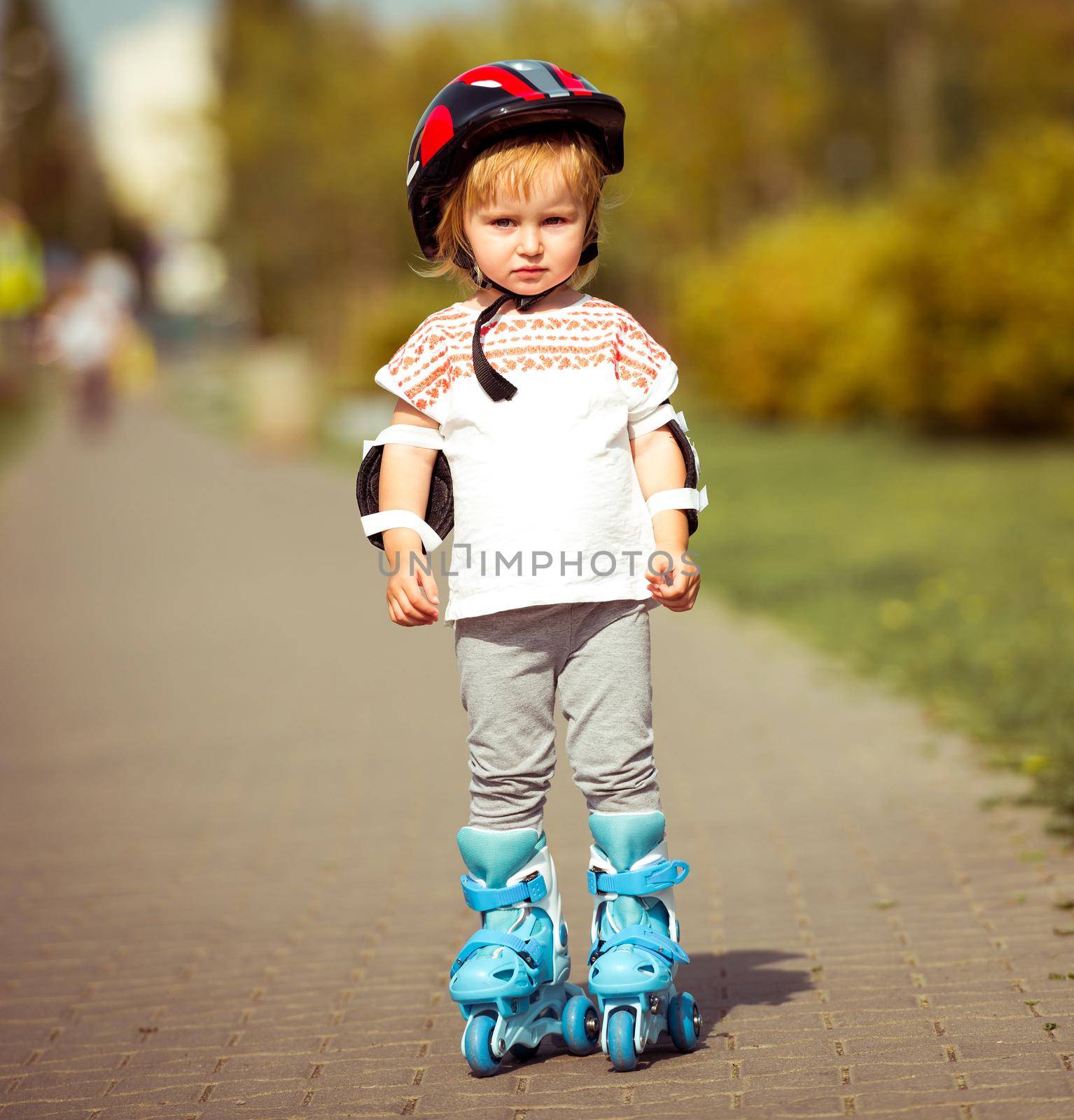 two year old pretty girl in roller skates and a helmet on the street