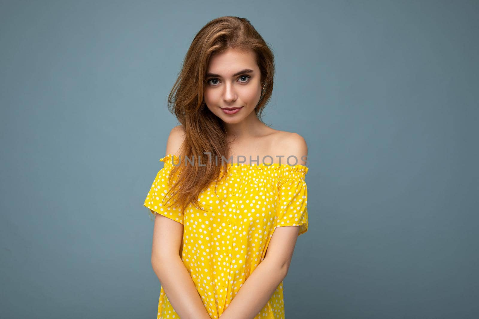 Young beautiful dark blonde woman with sincere emotions isolated on background wall with copy space wearing stylish summer yellow dress. Positive concept.