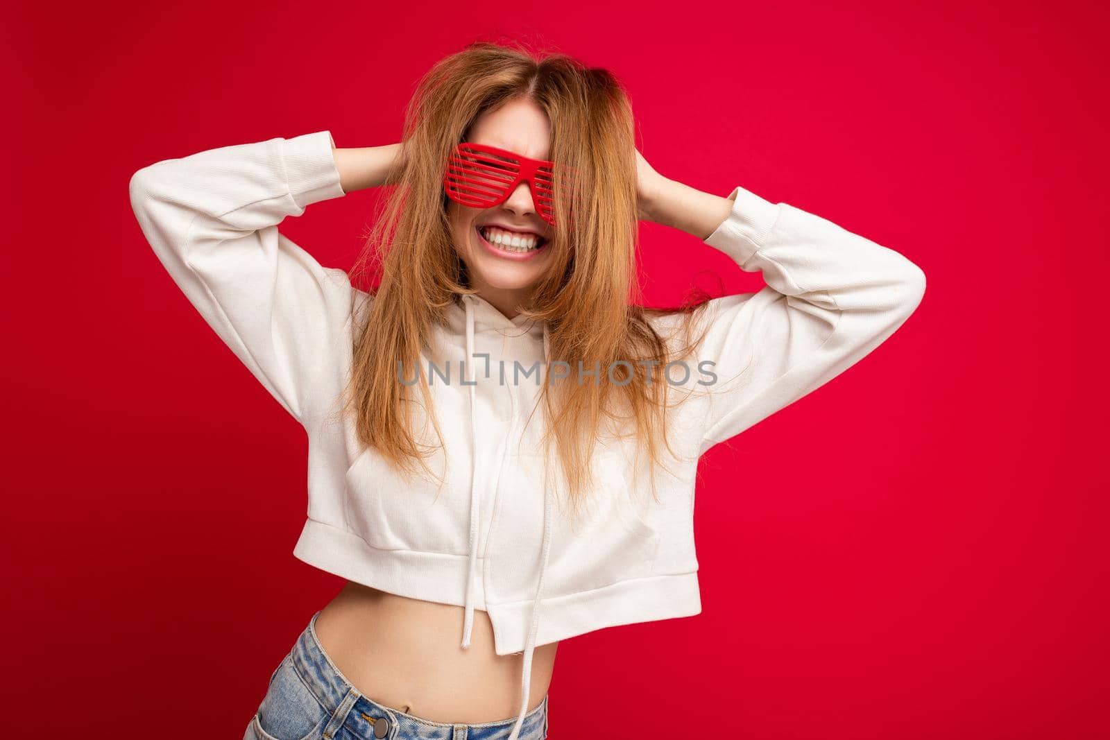 Photo shot of beautiful positive young blonde woman wearing casual clothes and stylish optical glasses isolated over colorful background wall looking at camera and having fun.