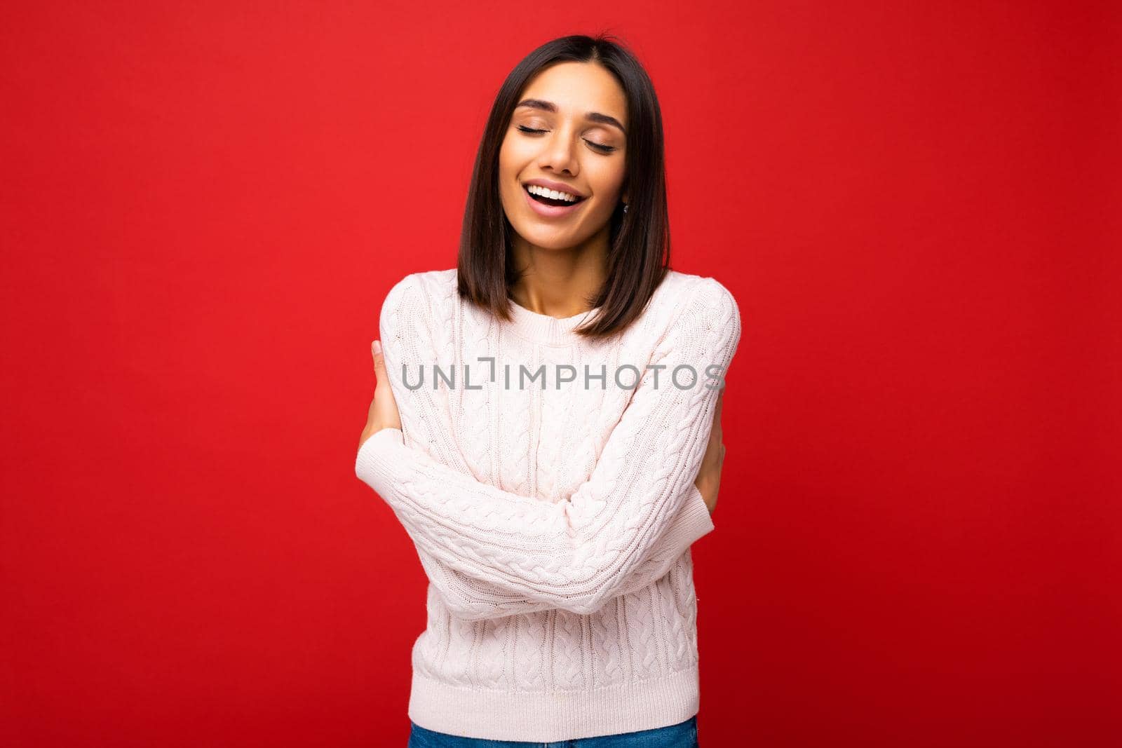 Portrait of positive cheerful cute smiling young brunette woman in casual sweater isolated on red background with copy space.