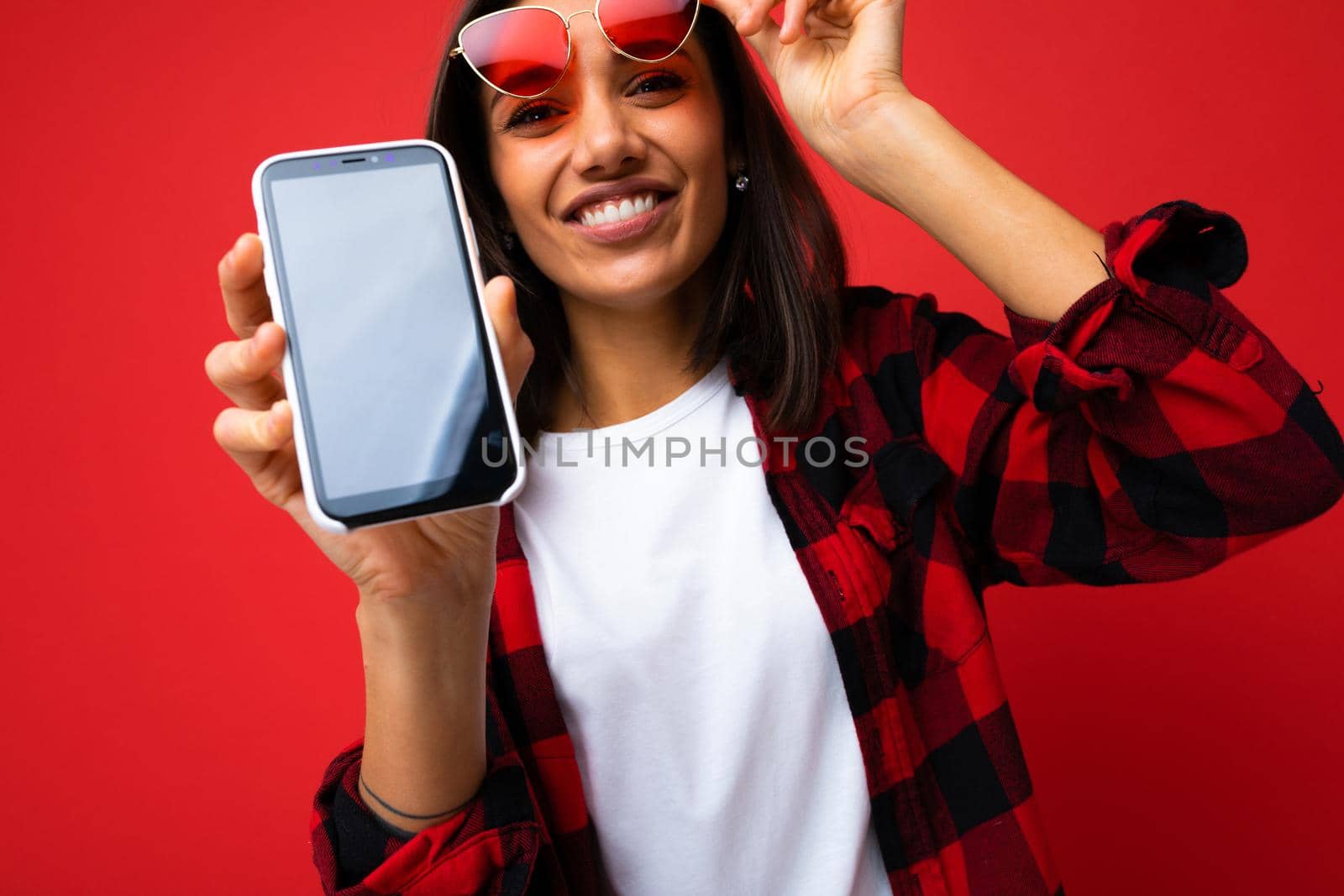 Surprised young woman posing isolated on red background, studio portrait. People lifestyle concept. Mock up copy space. Using mobile phone, typing sms message by TRMK