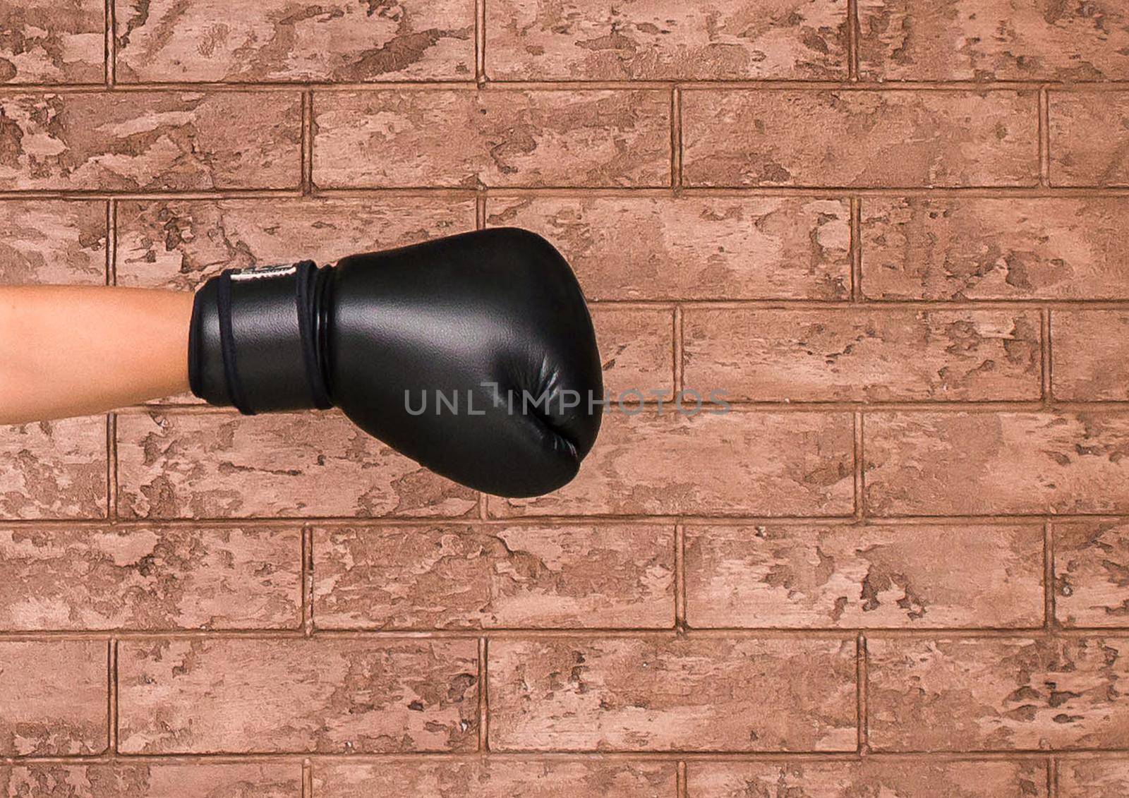 The hand of a guy in a black wrestling glove on a background of a brown brick wall. Boxing concept.