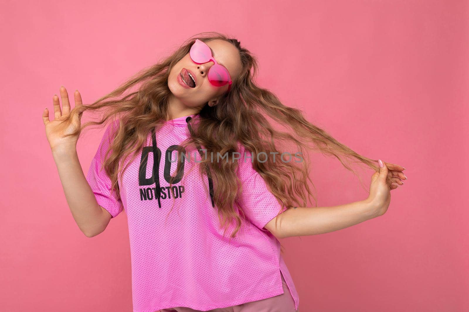 Attractive amusing joyful young blonde woman wearing everyday stylish clothes and modern sunglasses isolated on colorful background wall looking at camera,