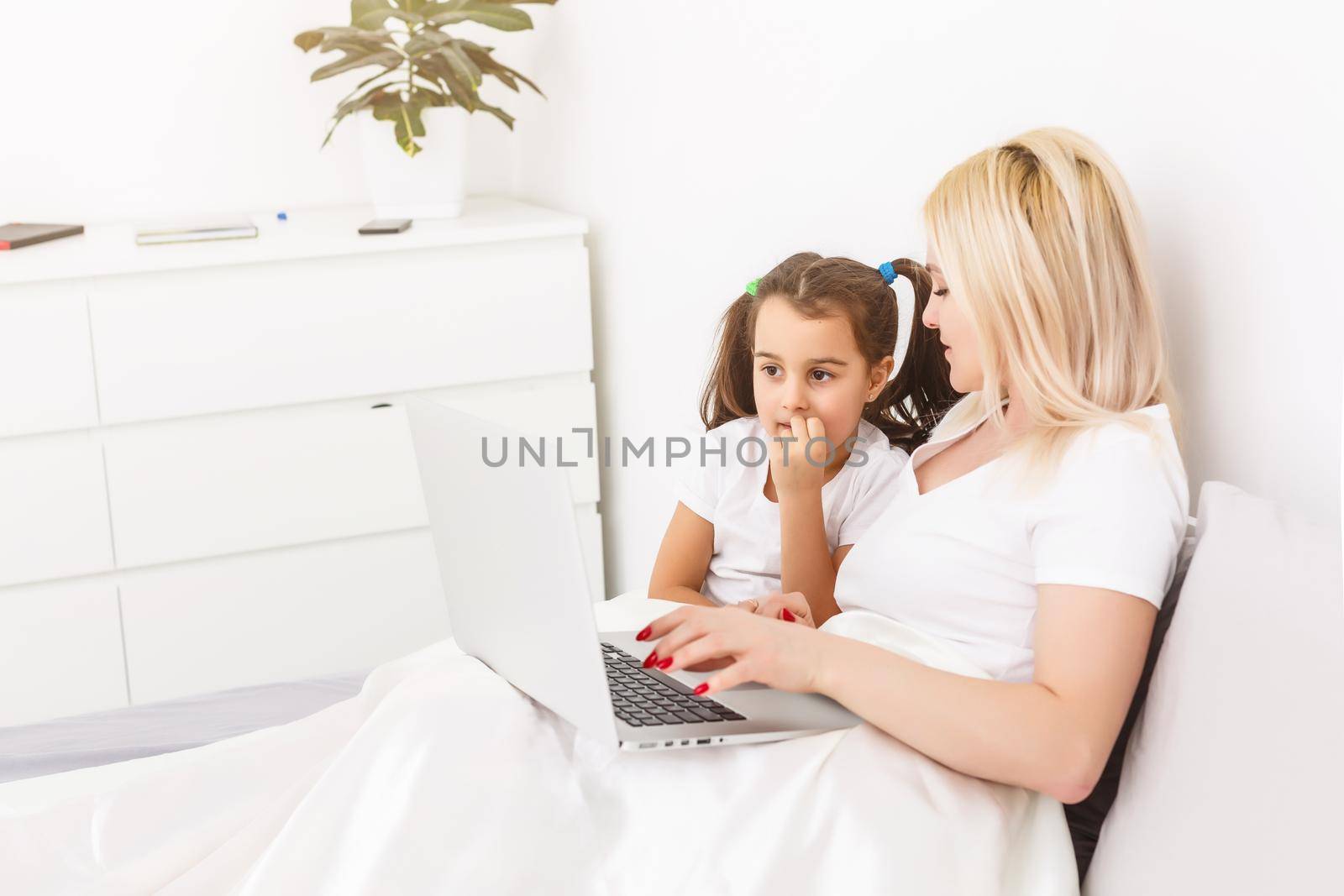 Smiling mother and daughter using laptop in bed at home by Andelov13