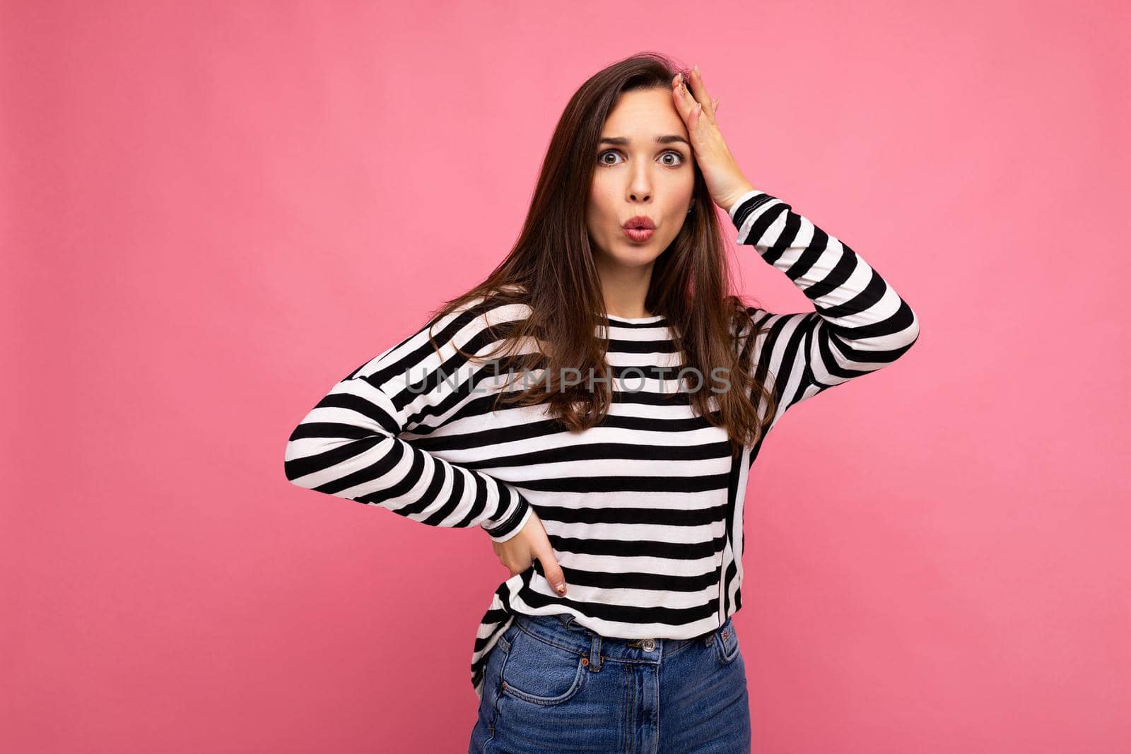 Photo of young astonished surprised beautiful brunette woman with sincere emotions wearing casual striped pullover isolated on pink background with copy space by TRMK