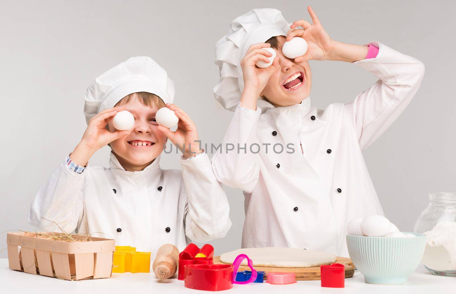 smiling little boy and girl in cook form holding eggs