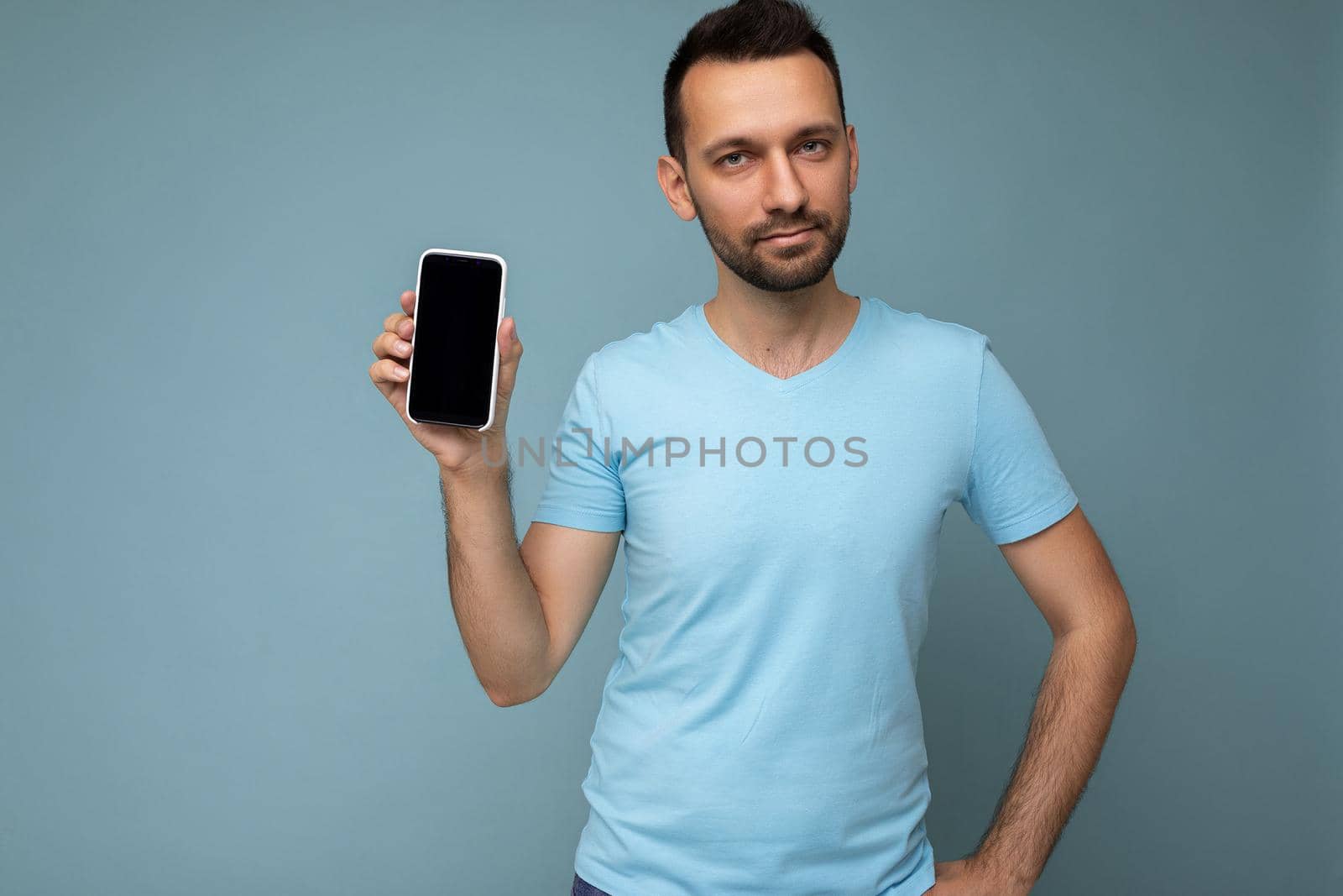 Handsome happy cool young man good looking wearing casual stylish clothes standing isolated over colourful background wall holding smartphone and showing phone with empty screen display looking at camera.