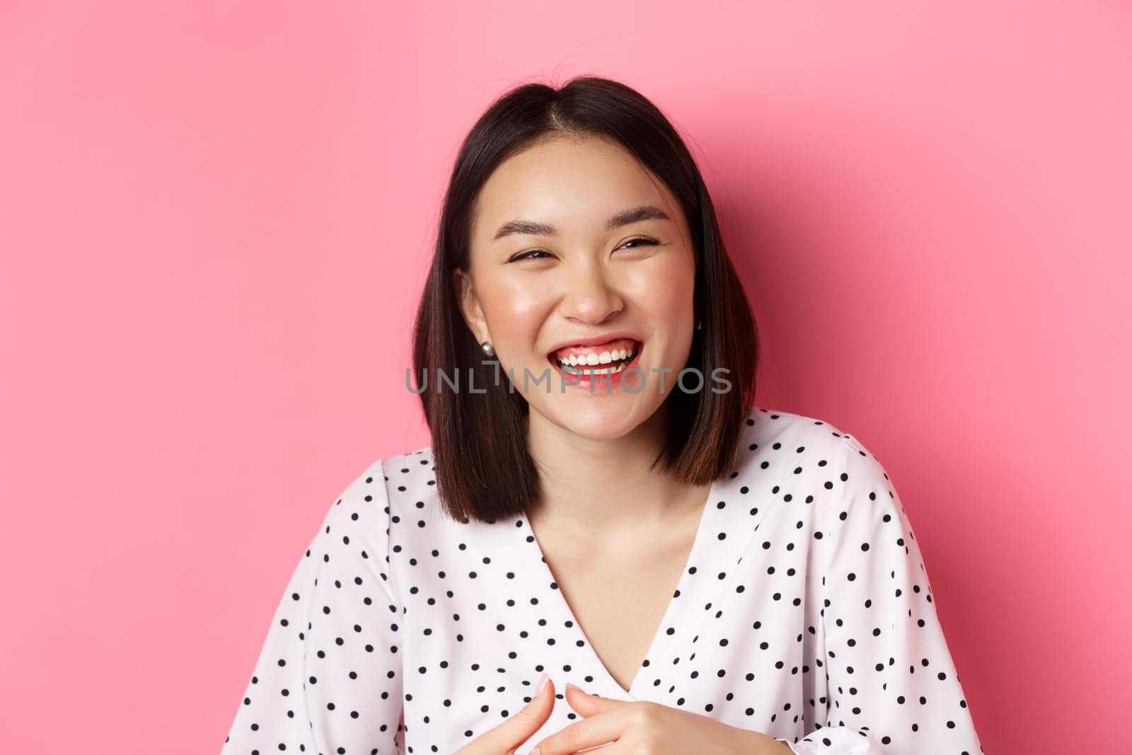 Beauty and lifestyle concept. Close-up of happy asian woman laughing and having fun, standing over pink background. Copy space