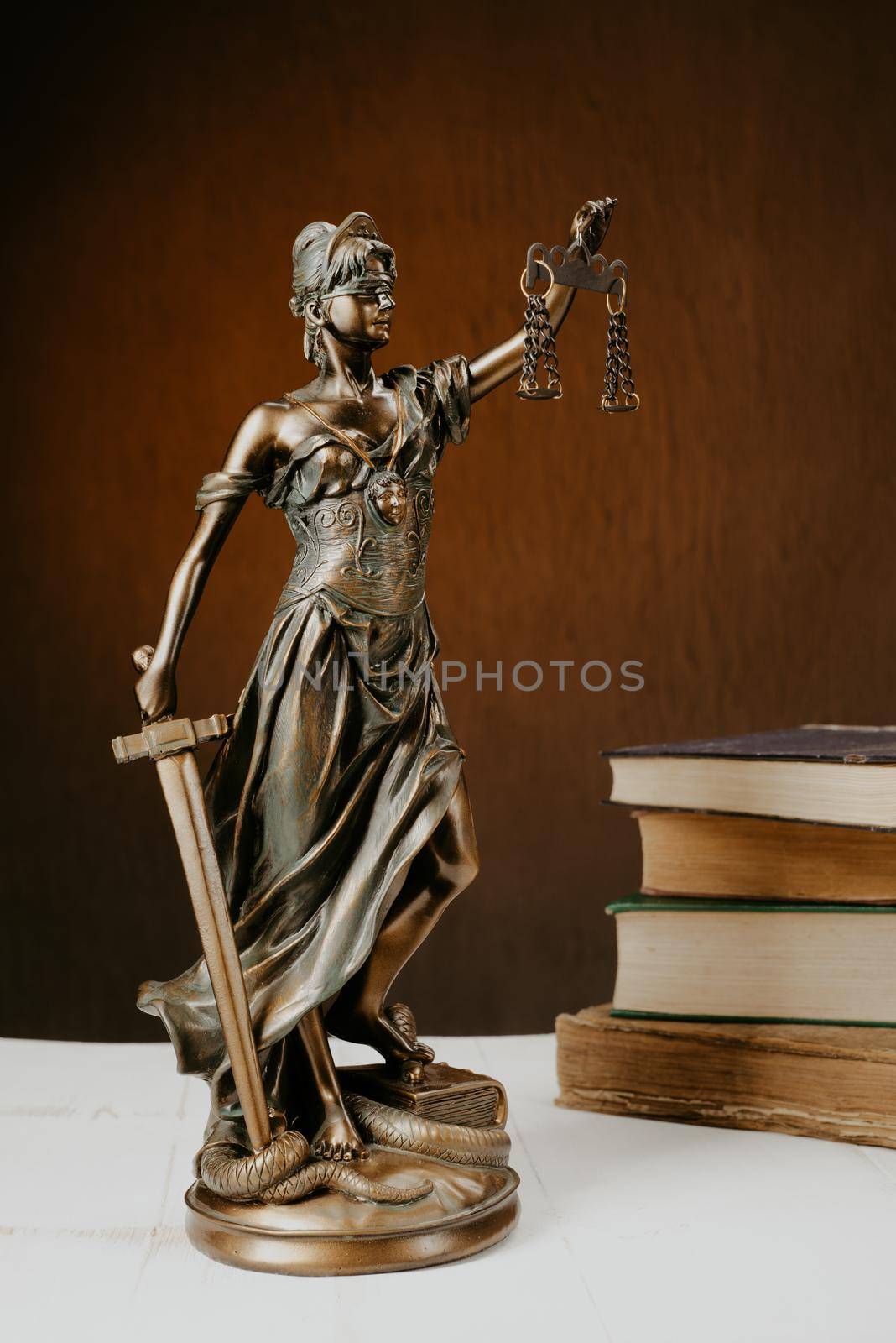 Themis figurine stands on a white wooden table next to a stack of old books. Scales Law Lawyer Business Concept. - Image