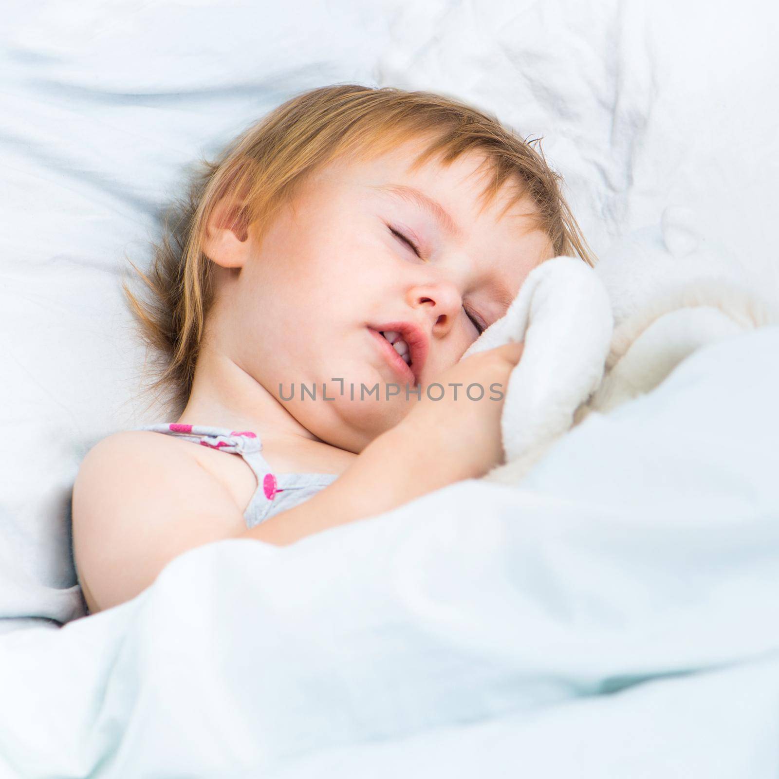 beautiful baby girl with a toys sleep in white bed
