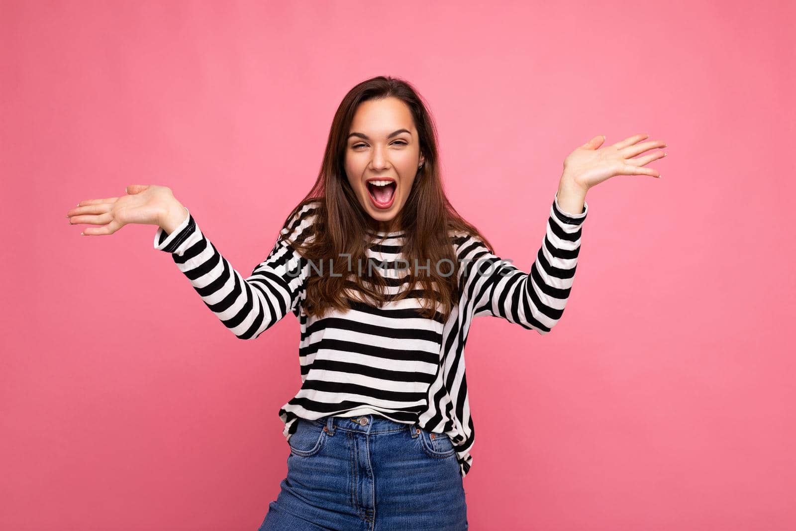 Portrait of young emotional positive shocked surprised happy beautiful brunette woman with sincere emotions in casual striped pullover isolated on pink background with copy space.