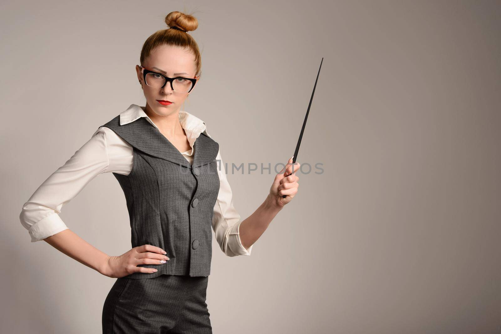 slim serious young woman teacher in suit with pointer in hand. Beautiful girl near the white wall