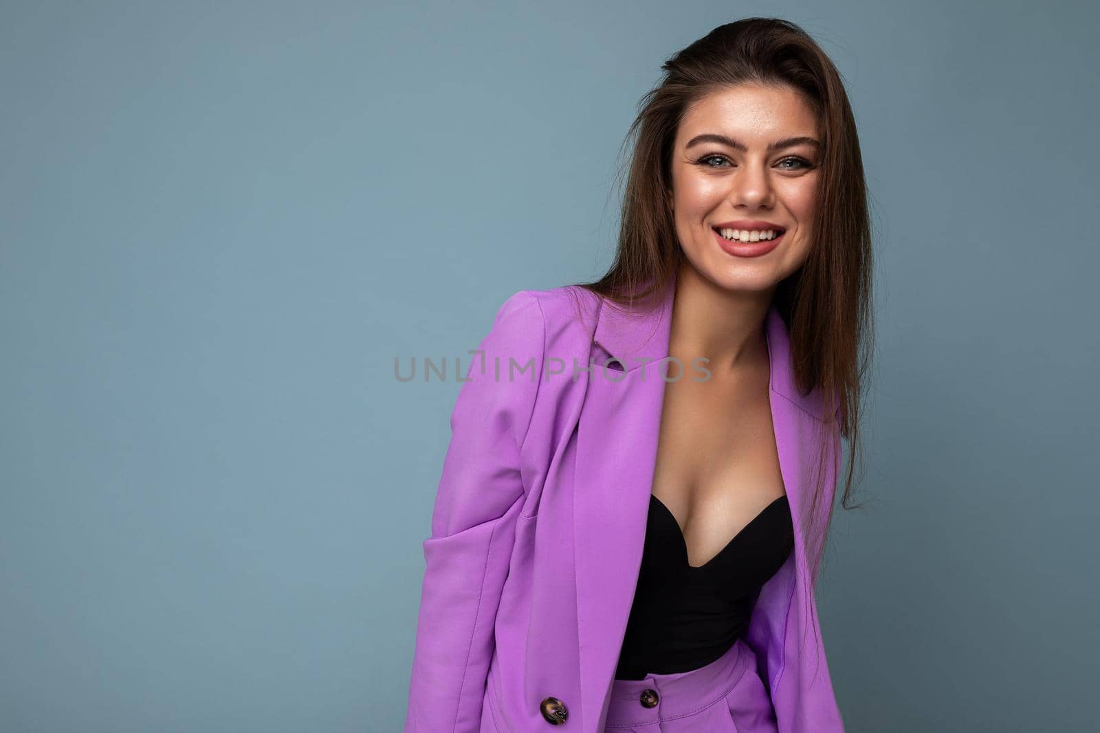Young happy smiling brunette woman nice-looking attractive charming elegant fashionable wearing stylish suit with jacket isolated over blue background with copy space. Fun anf joy concept.
