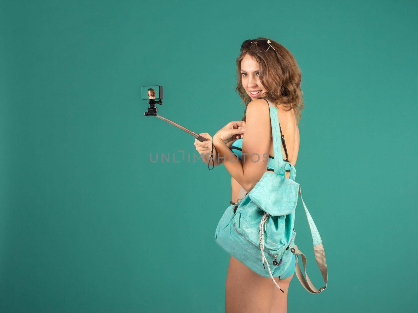 Hipster girl making selfie with action camera on green background wearing swimwear.