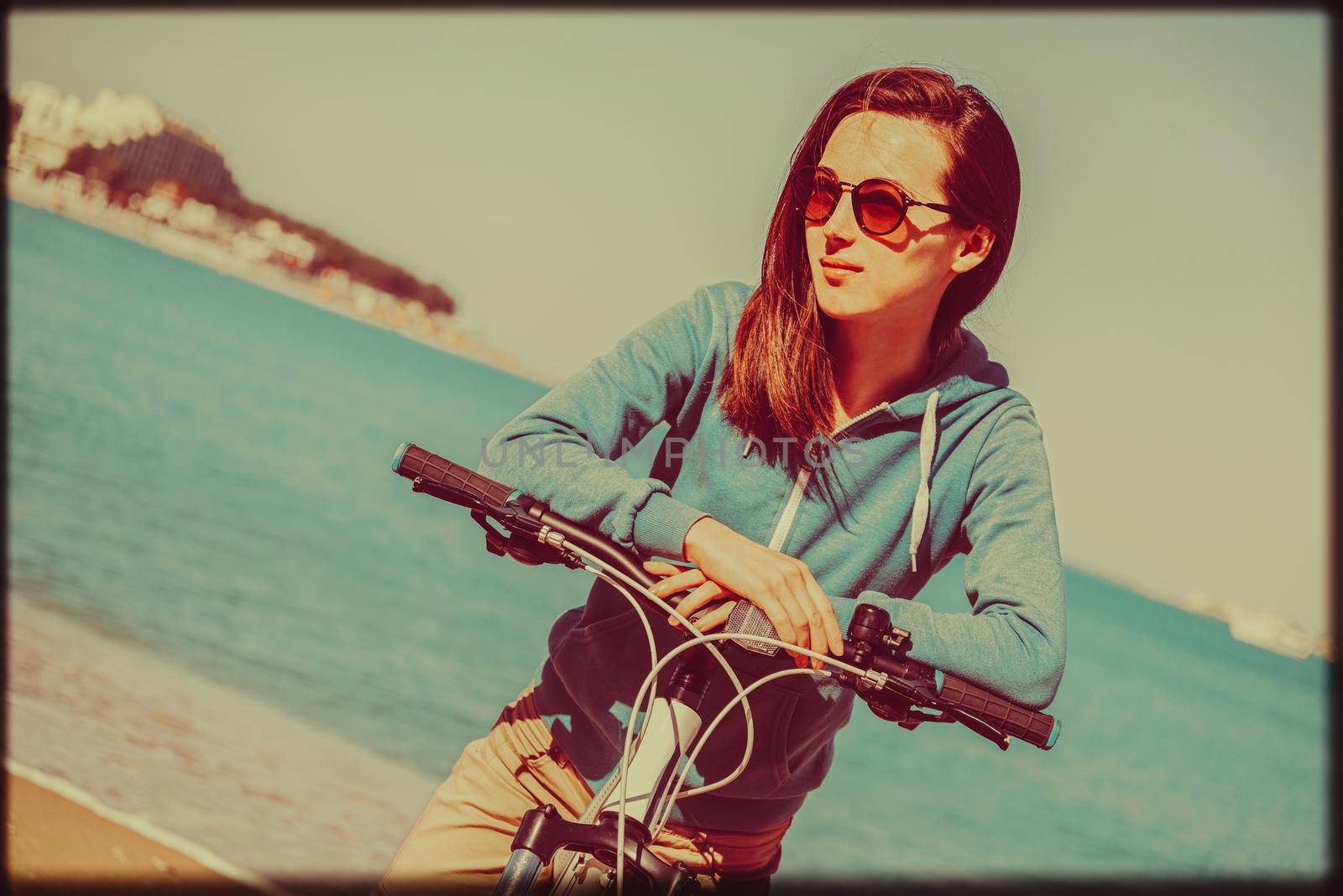 Smiling beautiful young woman with a bicycle on beach in summer. Image with vintage color effect and rectangular frame