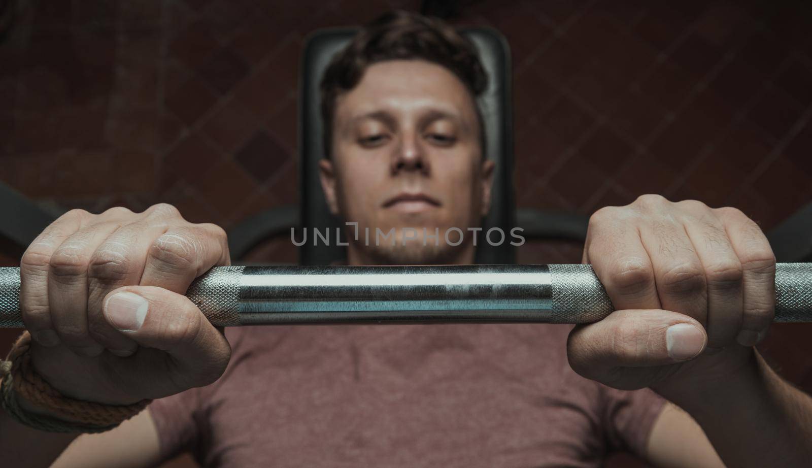 Muscular man lifting a barbell on bench at gym, top view