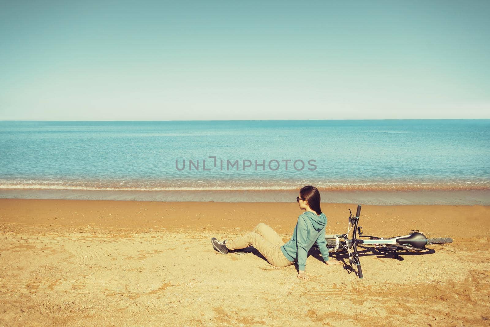 Beautiful young woman resting near a bicycle on beach in summer