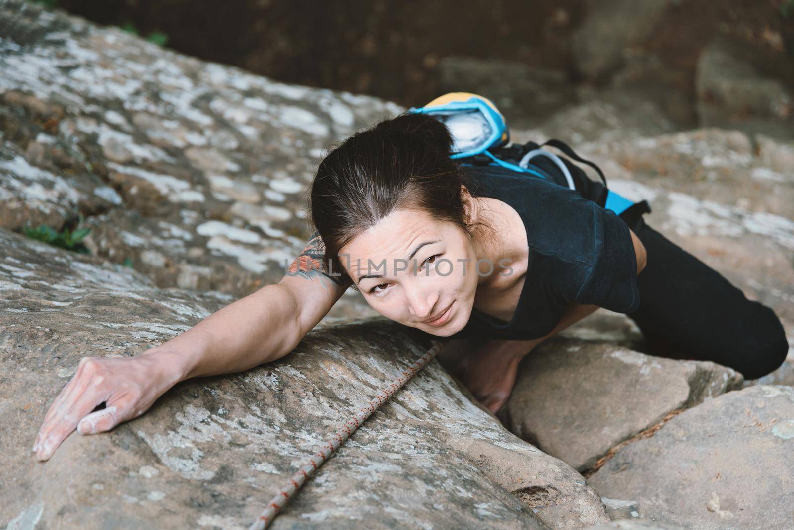Beautiful young woman in safety equipment climbing on stone rock, top view