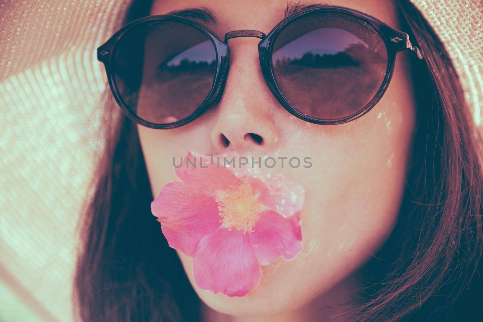 Portrait of attractive girl in sunglasses with pink flower, concept of summer mood. Fashionable and beautiful summer girl. Image with instagram color effect