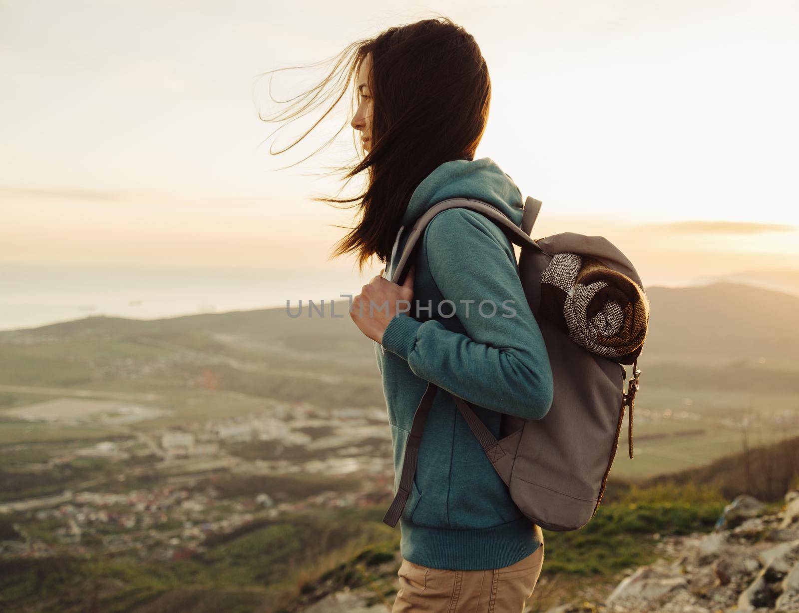 Hiker young woman with backpack standing on peak of mountain in summer at sunset