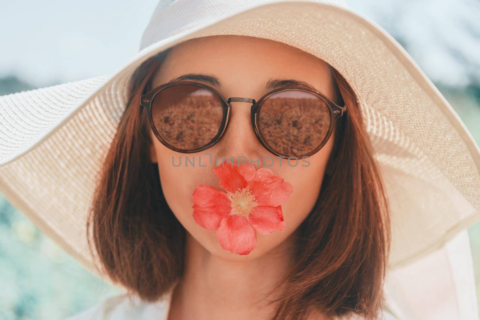 Portrait of young woman in sunglasses and hat with red flower, concept of summer mood. Fashionable and beautiful summer girl