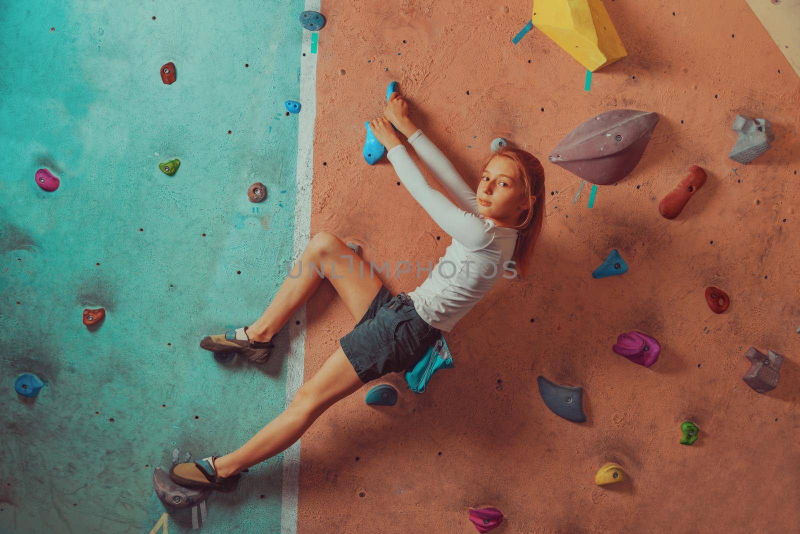 Sporty little girl climbing artificial boulder on practical wall in gym, concept of healthy lifestyle