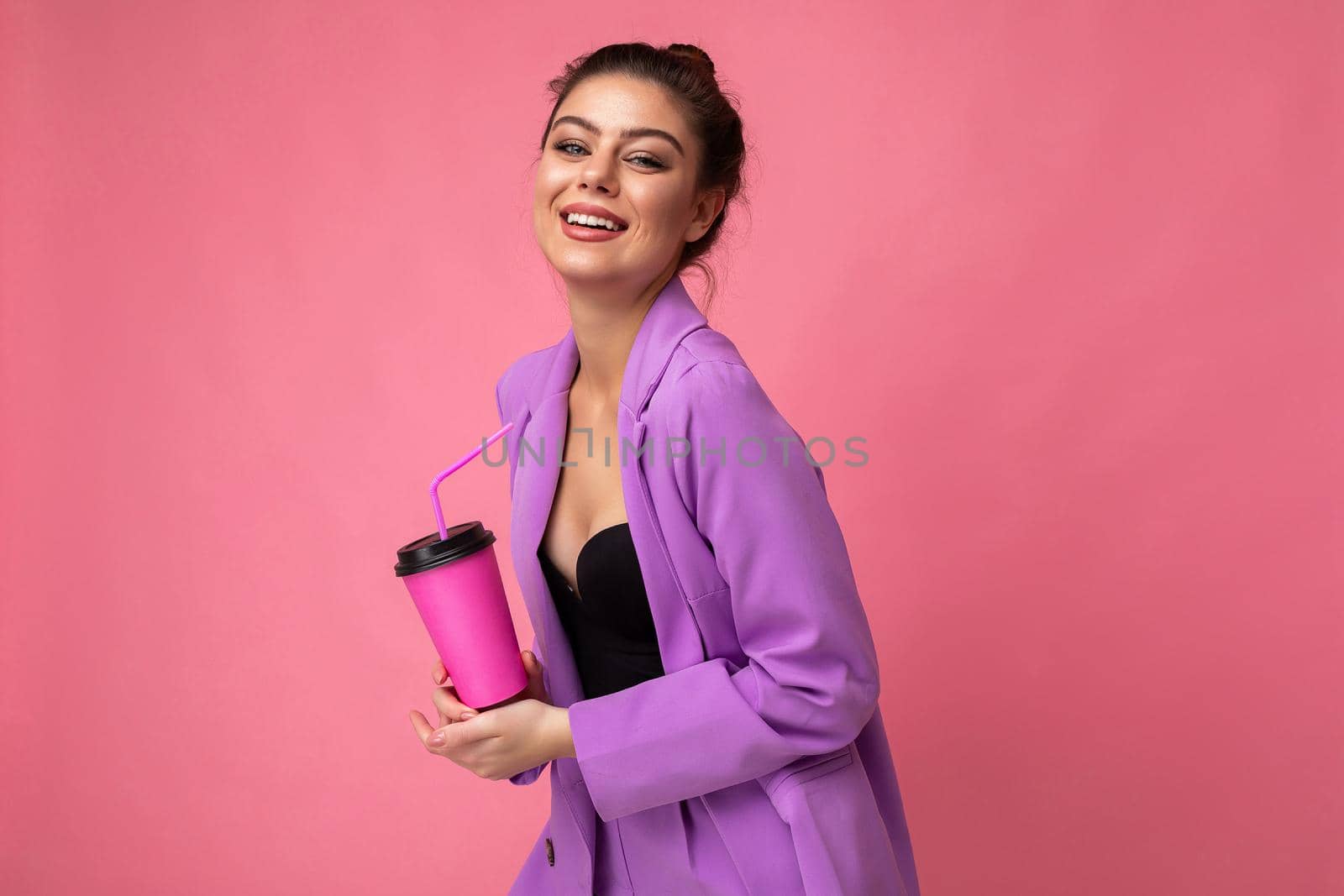Beautiful young positive brunette woman wearing casual stylish clothes isolated over colorful background wall holding paper cup for mockup drinking coffee looking at camera. copy space