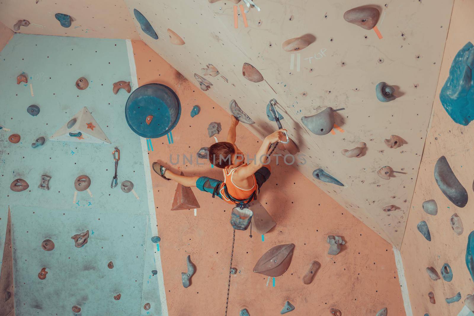 Boy in harness and safety equipment climbing on practical wall indoor