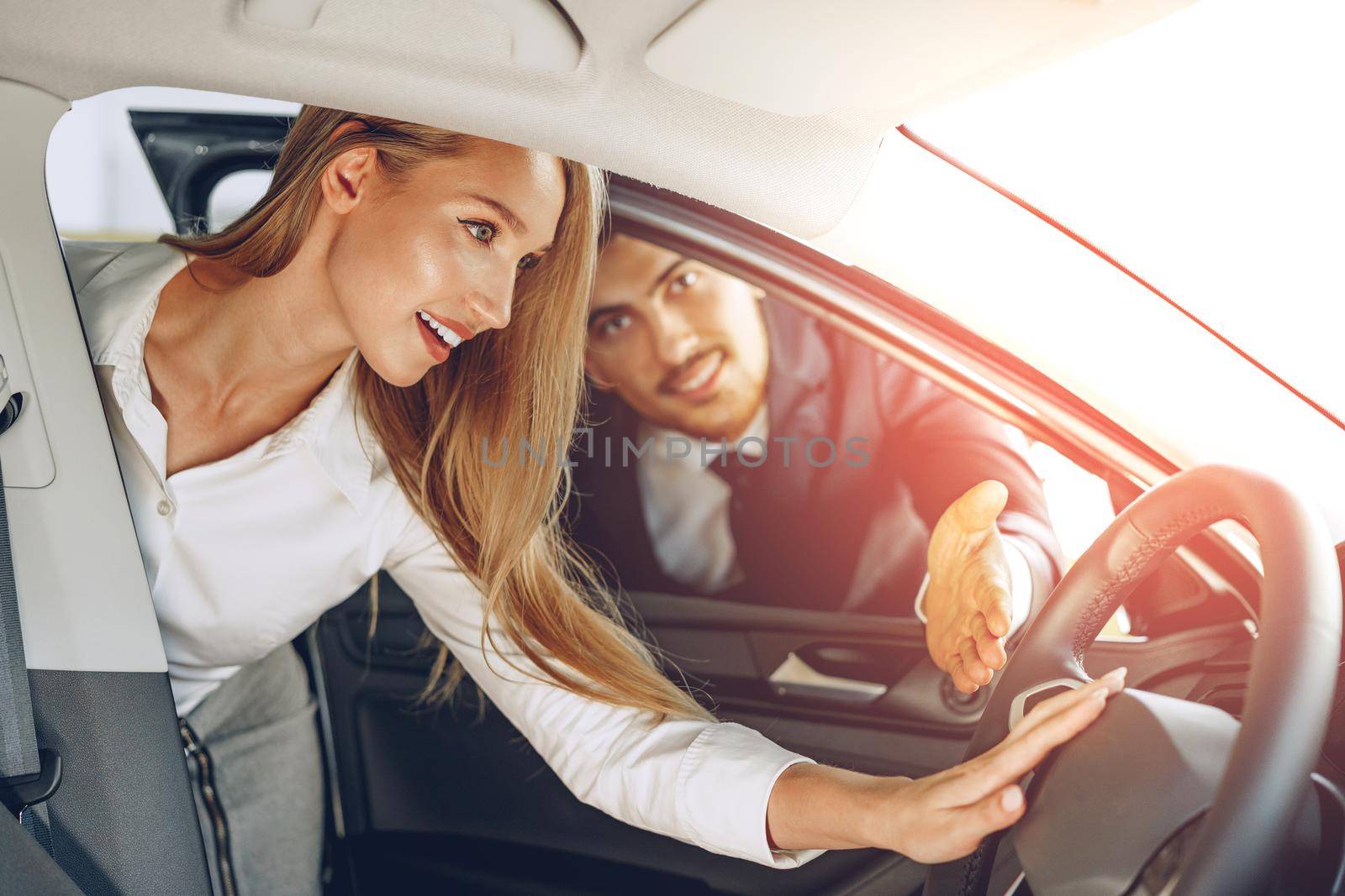 Man car dealer showing a woman buyer a new car in car salon