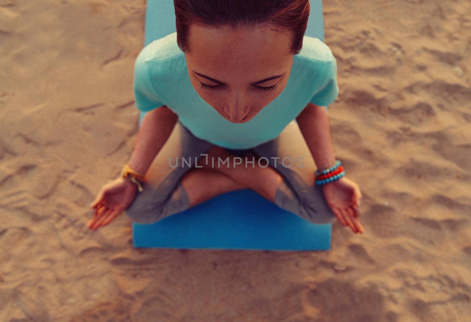 Young woman meditating in pose of lotus on beach, top view