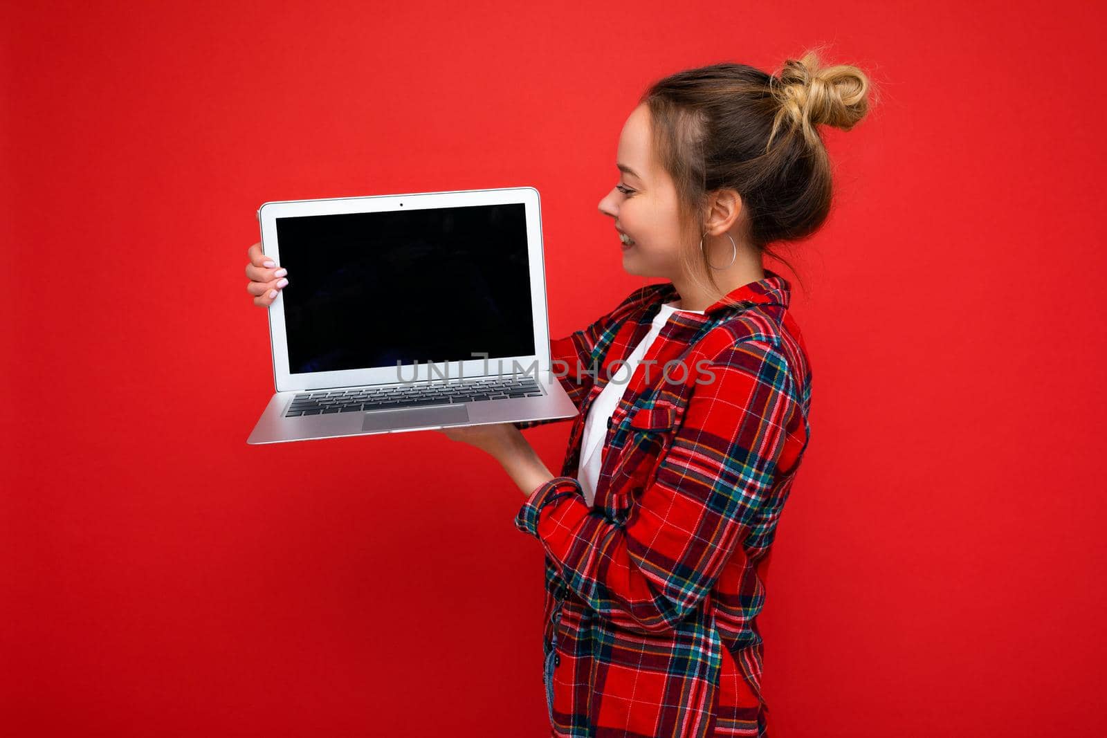 side profile photo of charming pretty young lady holding netbook looking at screen wearing red shirt isolated over red wall background.
