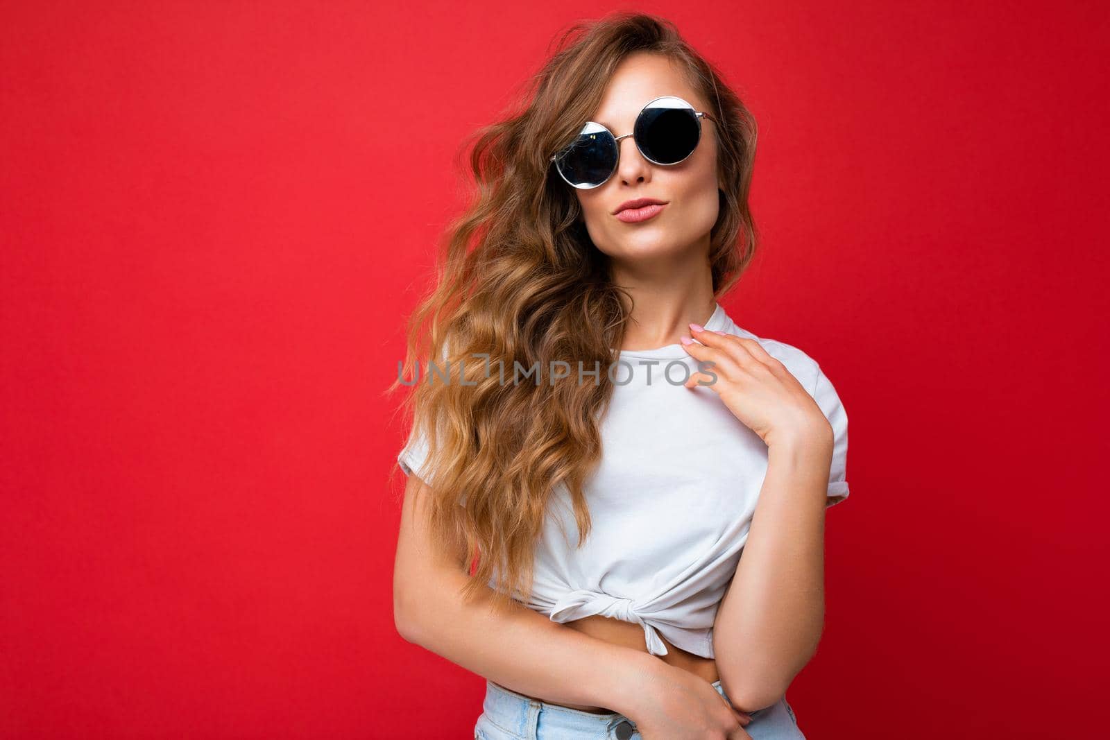 Photo shot of beautiful young blonde woman wearing casual clothes and stylish sunglasses isolated over colorful background looking at camera. copy space