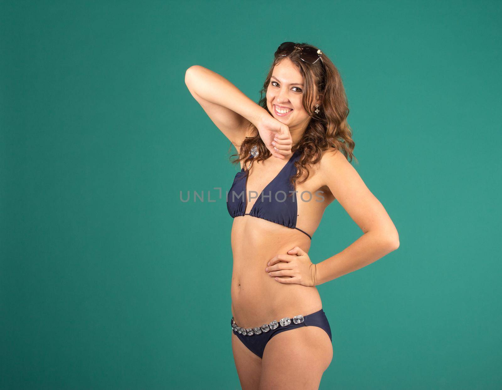 Happy young woman in blue bikini swimsuit posing on green background