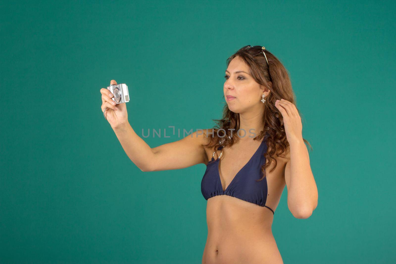 Travel concept. Studio portrait of pretty young woman taking image with camera on green background