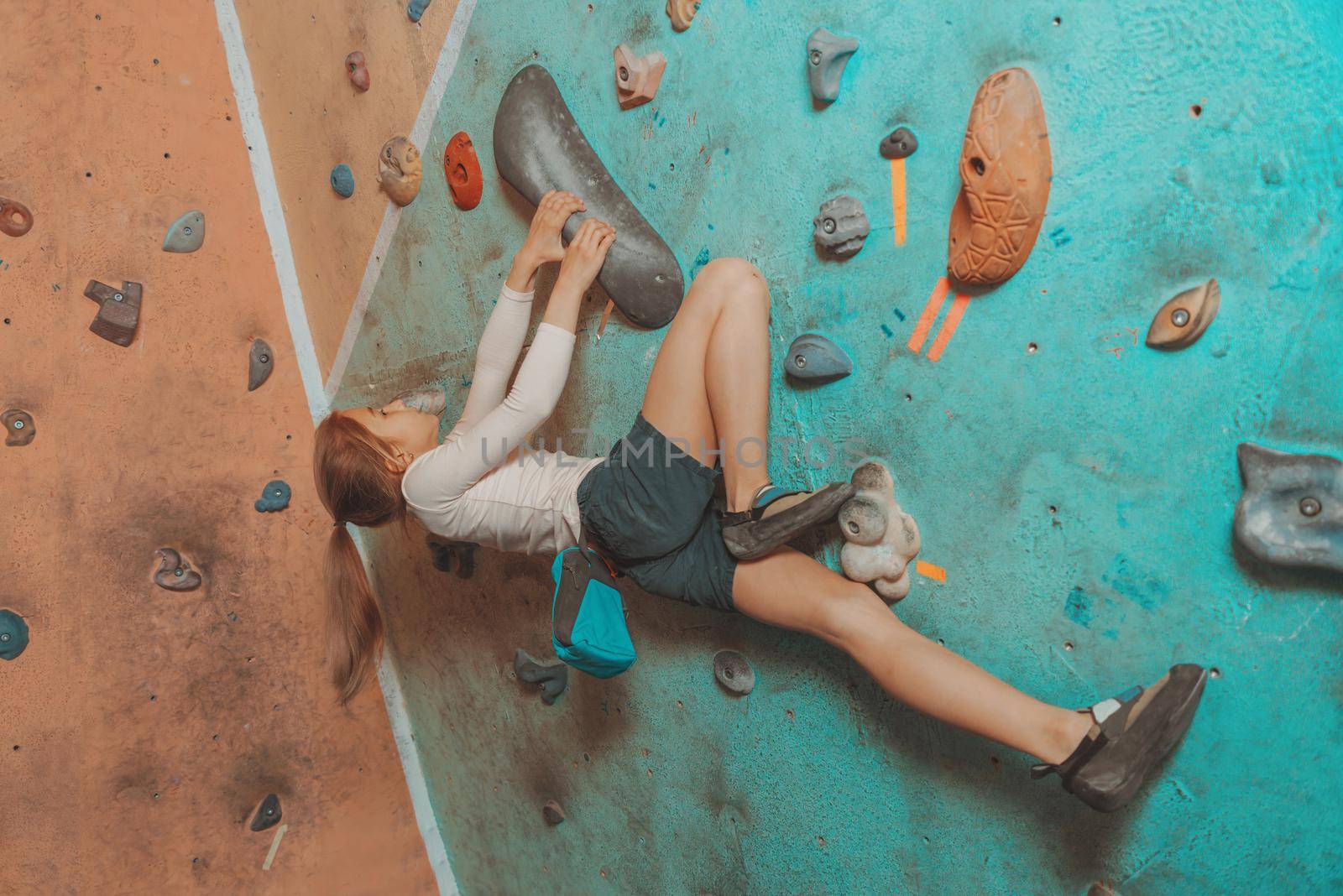 Climber little sporty girl exercises on artificial boulders wall indoor