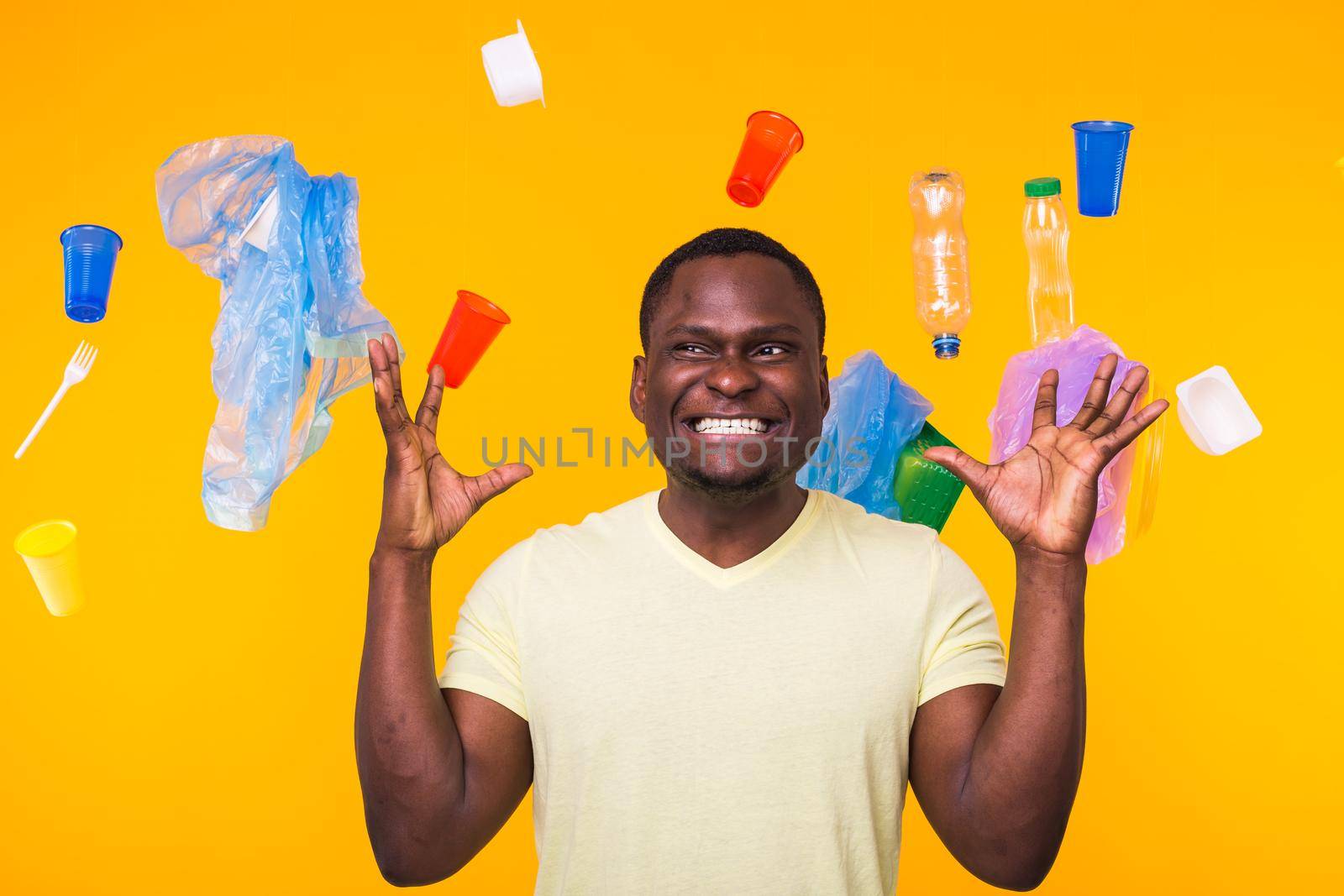 Plastic recycling problem, ecology and environmental disaster concept - Surprised african american man on yellow background with trash. He's worried about ecology disaster