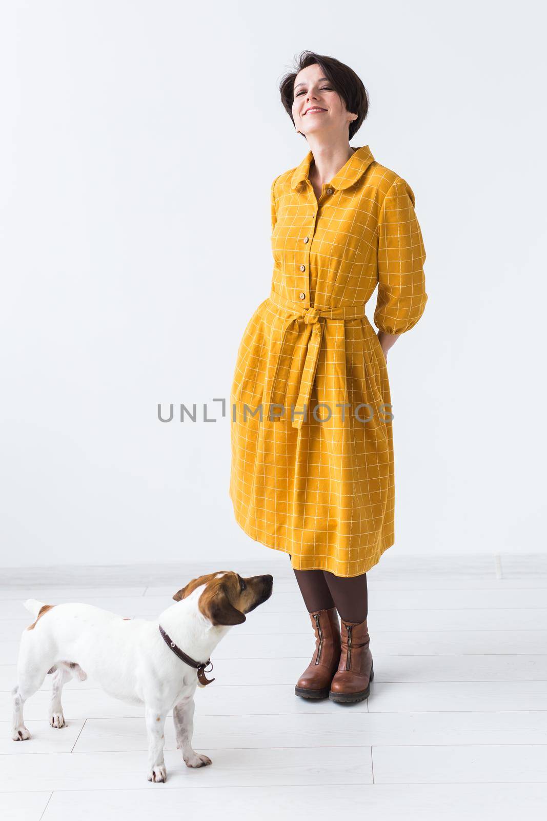 Cheerful young woman posing in a yellow dress with her beloved dog Jack Russell Terrier standing on a white background. The concept of casual wear. by Satura86