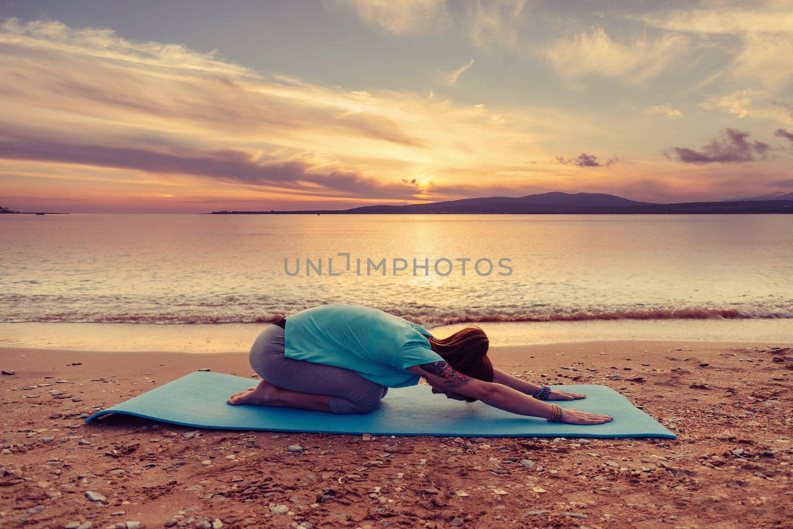 Young woman doing yoga exercise on summer beach near the sea at sunset, woman stretching her back