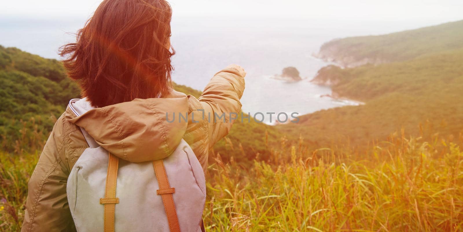 Hiker young woman with backpack pointing to the island in summer. Image with sunlight effect