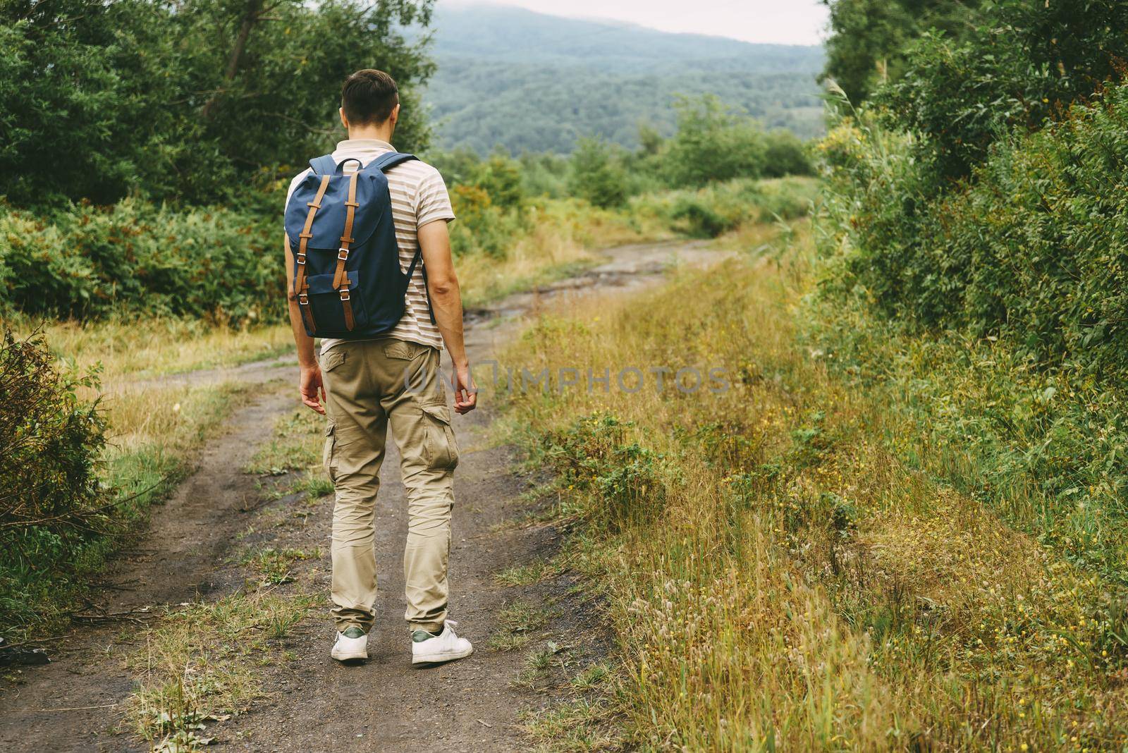 Hiker young man with backpack walking on footpath in summer forest