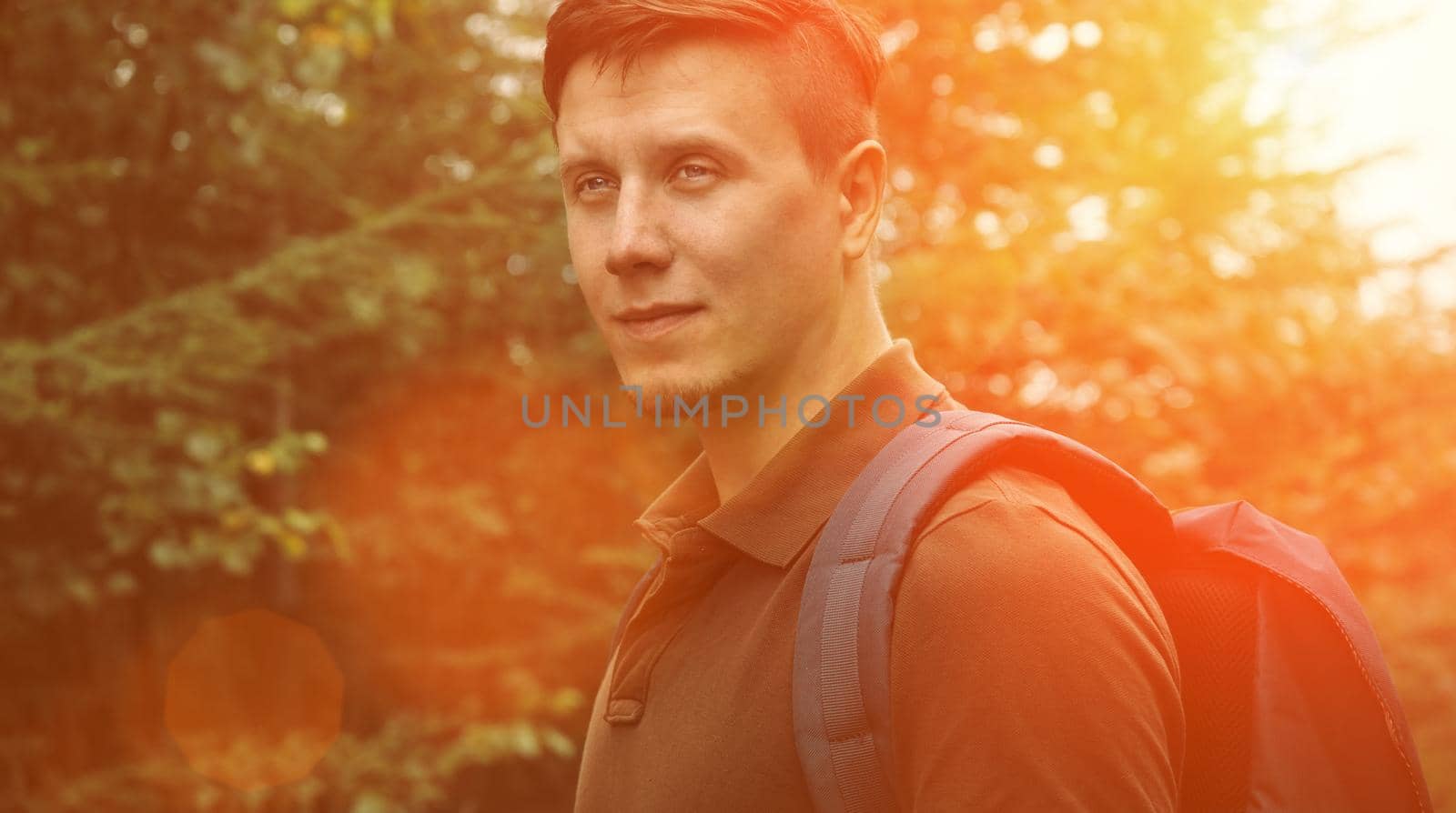 Smiling hiker young man walking in summer forest at sunny day. Image with sunlight effect