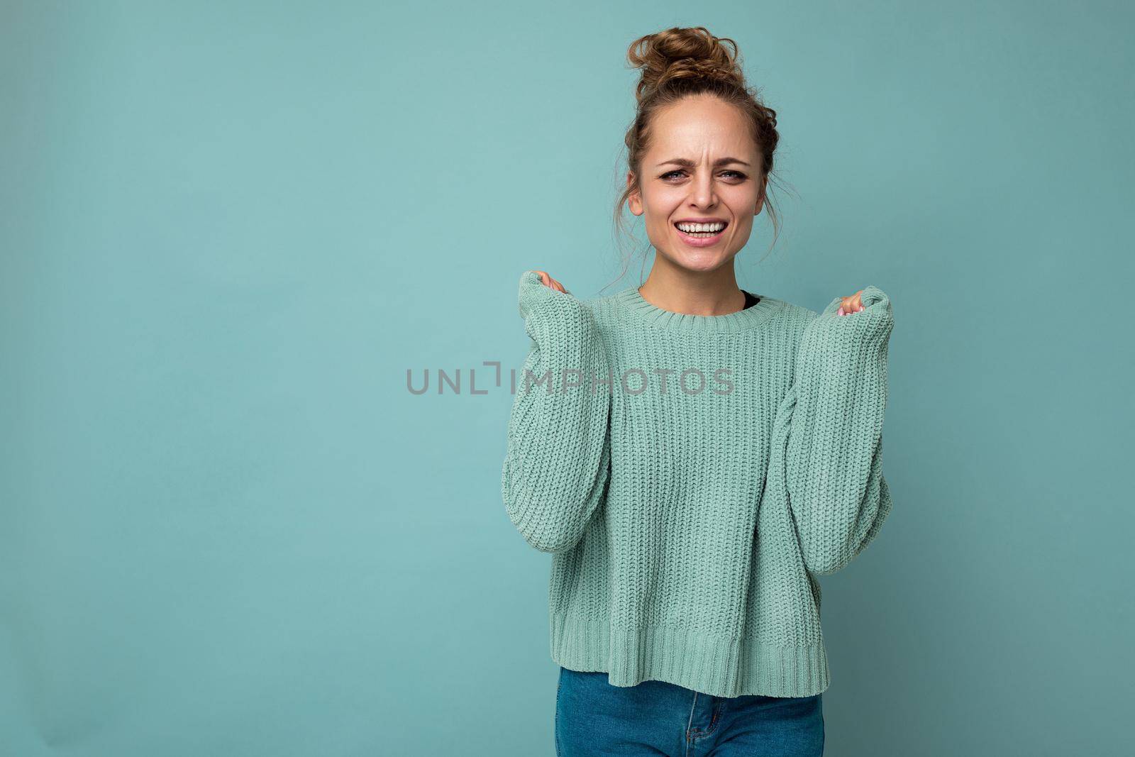 Portrait of young beautiful smiling hipster woman in trendy outfit. Sexy carefree female person posing isolated near blue wall in studio with free space. Positive model with natural makeup.